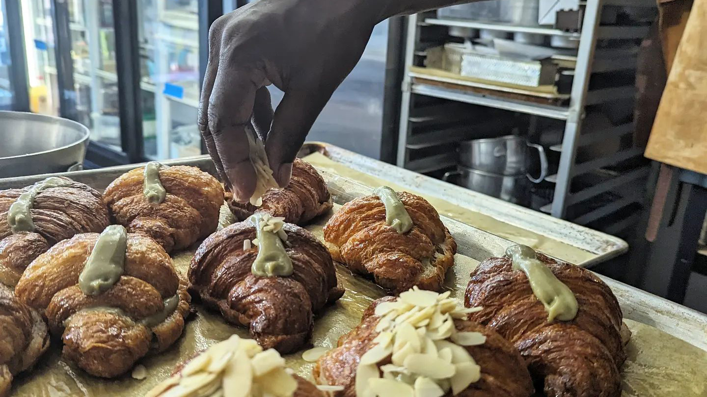 Chef sprinkling slivered almonds on top of fresh almond croissants