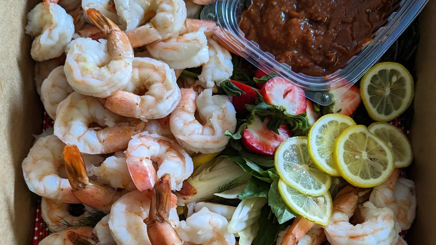 Catering spread of steamed and peeled shrimp with homemade sauce and lemon slices.