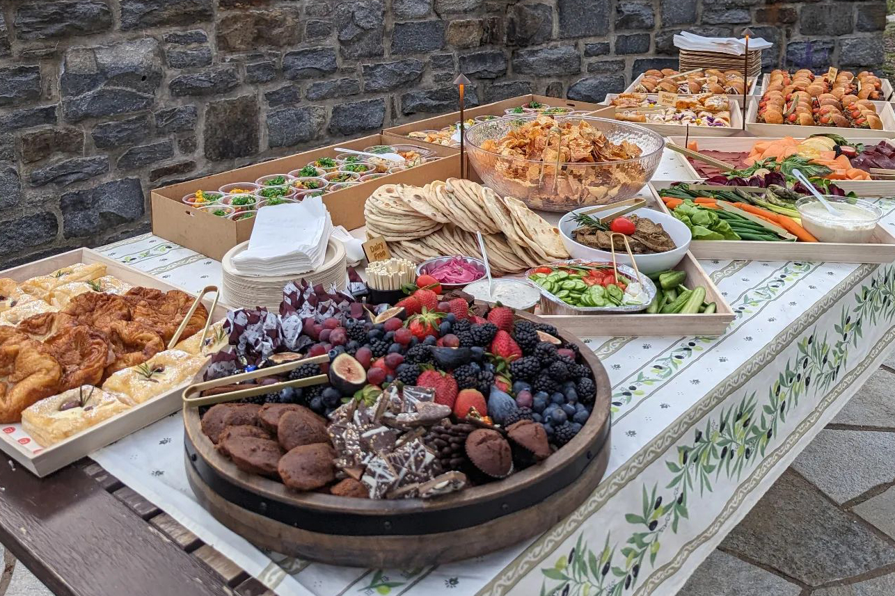 Outdoor catering spread of fresh pastries, crudités, sandwiches, and dessert.