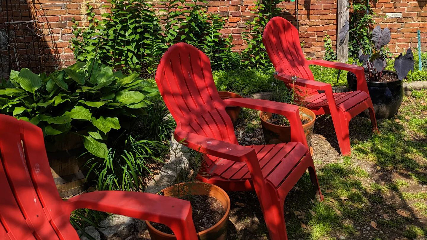 Three red Adirondack chairs in a garden